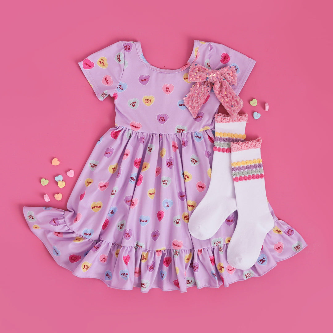 girls conversation heart inspired Valentine's dress with positive phrases, matching pastel stripe socks and pink velvet bow with sequins
