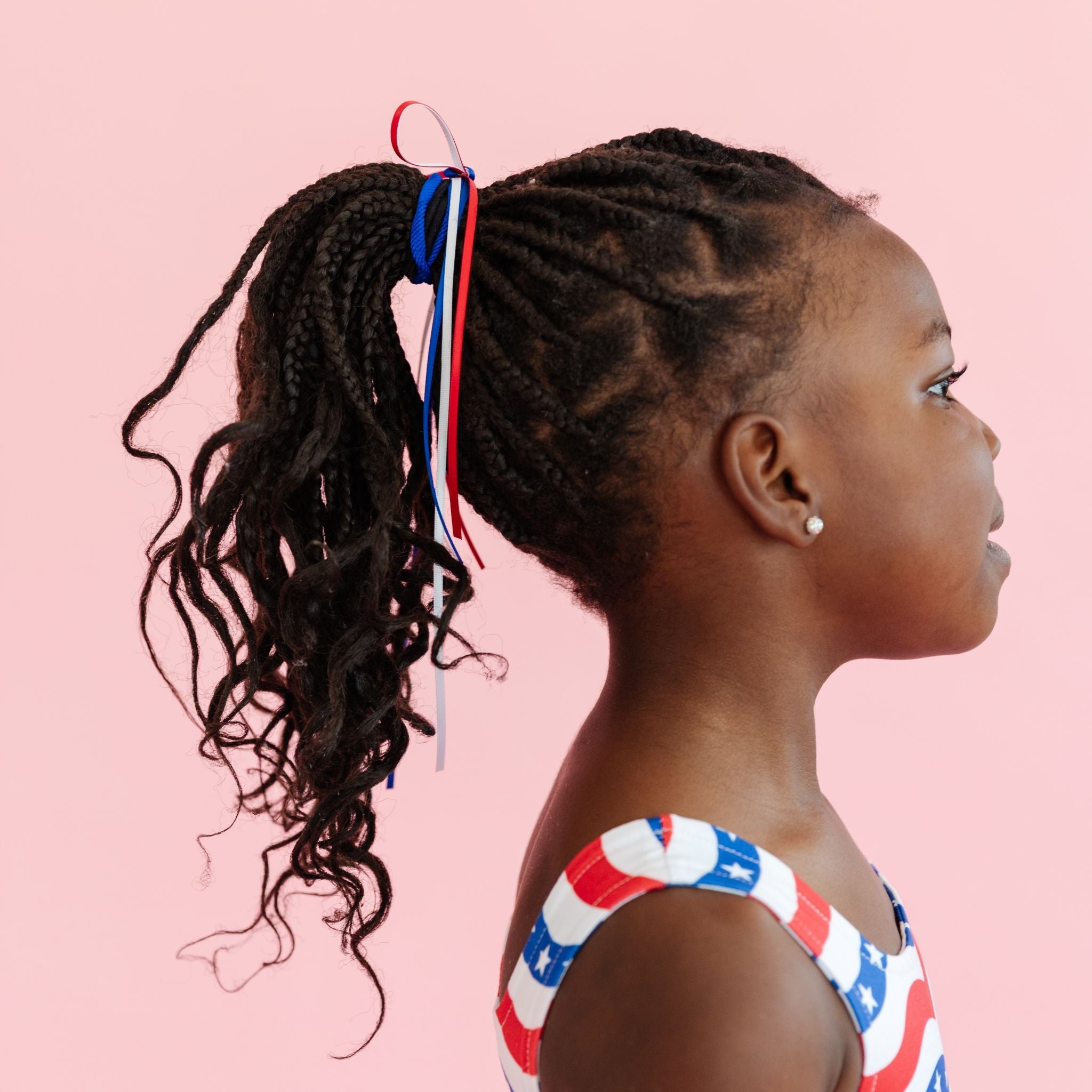 little girl in stars and stripes dress with matching red, white and blue ribbons tied to ponytail for 4th of July outfits