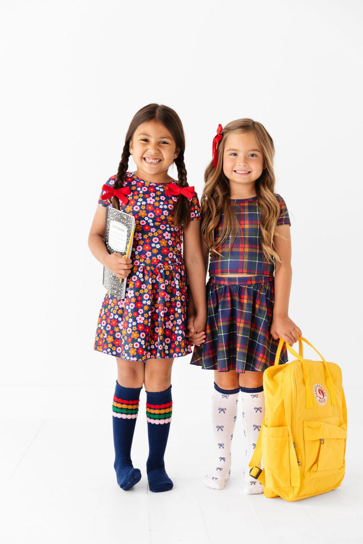little girls with backpack and books in matching floral and plaid skort and t-shirt sets for back to school paired with coordinating knee highs and bows