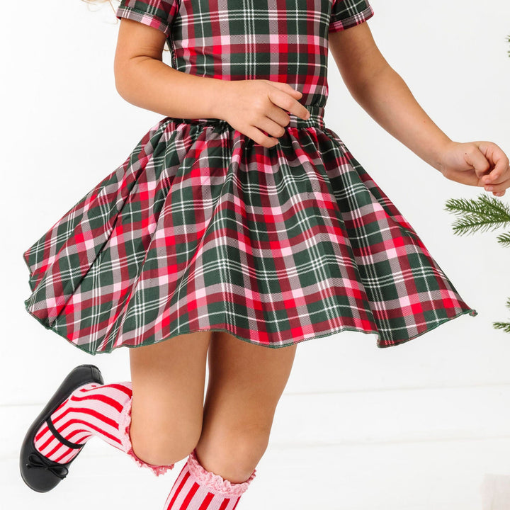 little girl twirling in green, red and pink Christms plaid top and skirt paired with red and pink striped knee high socks with lace