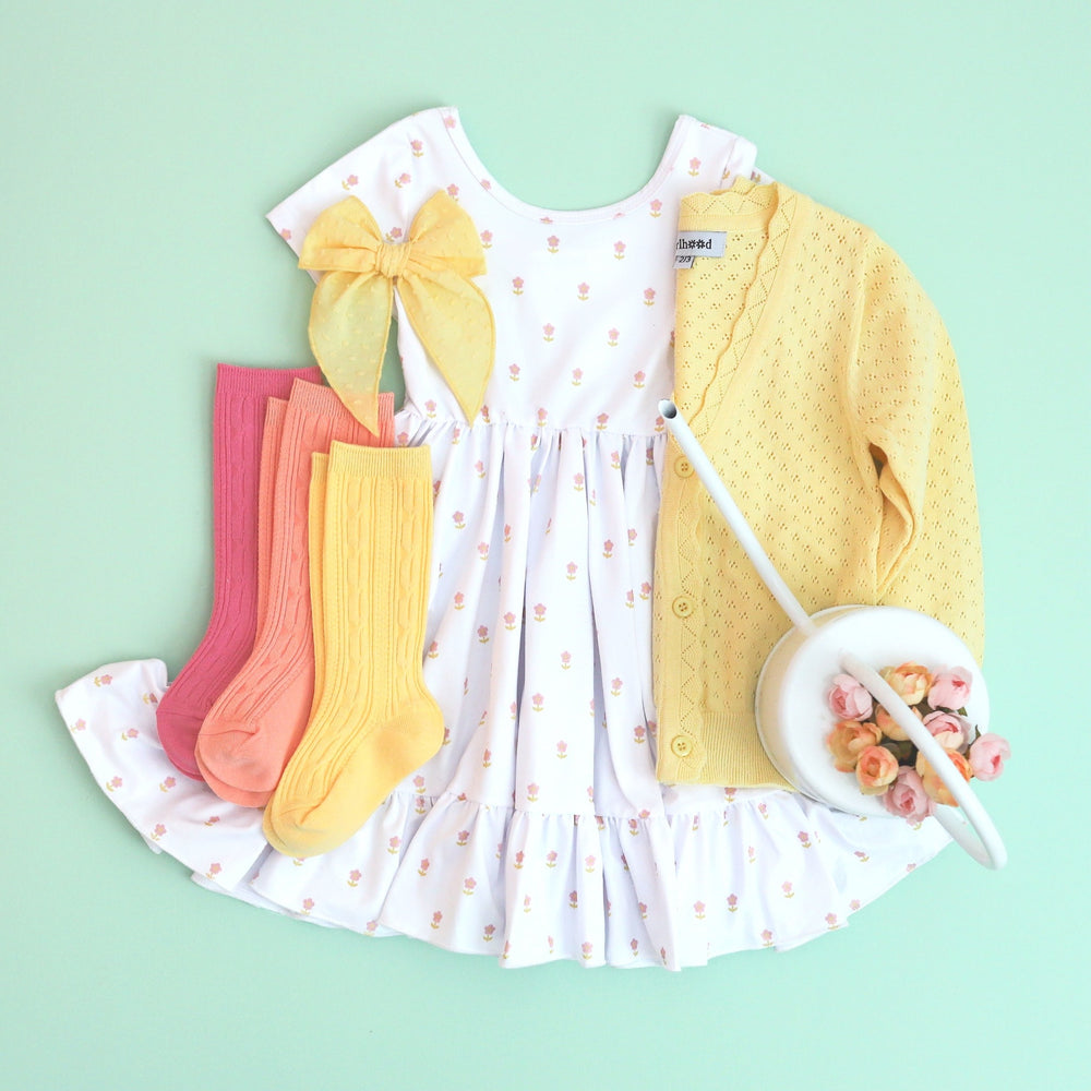 girls white twirl dress with dainty micro flowers paired with sherbet colored cable knit knee socks and a yellow crochet sweater