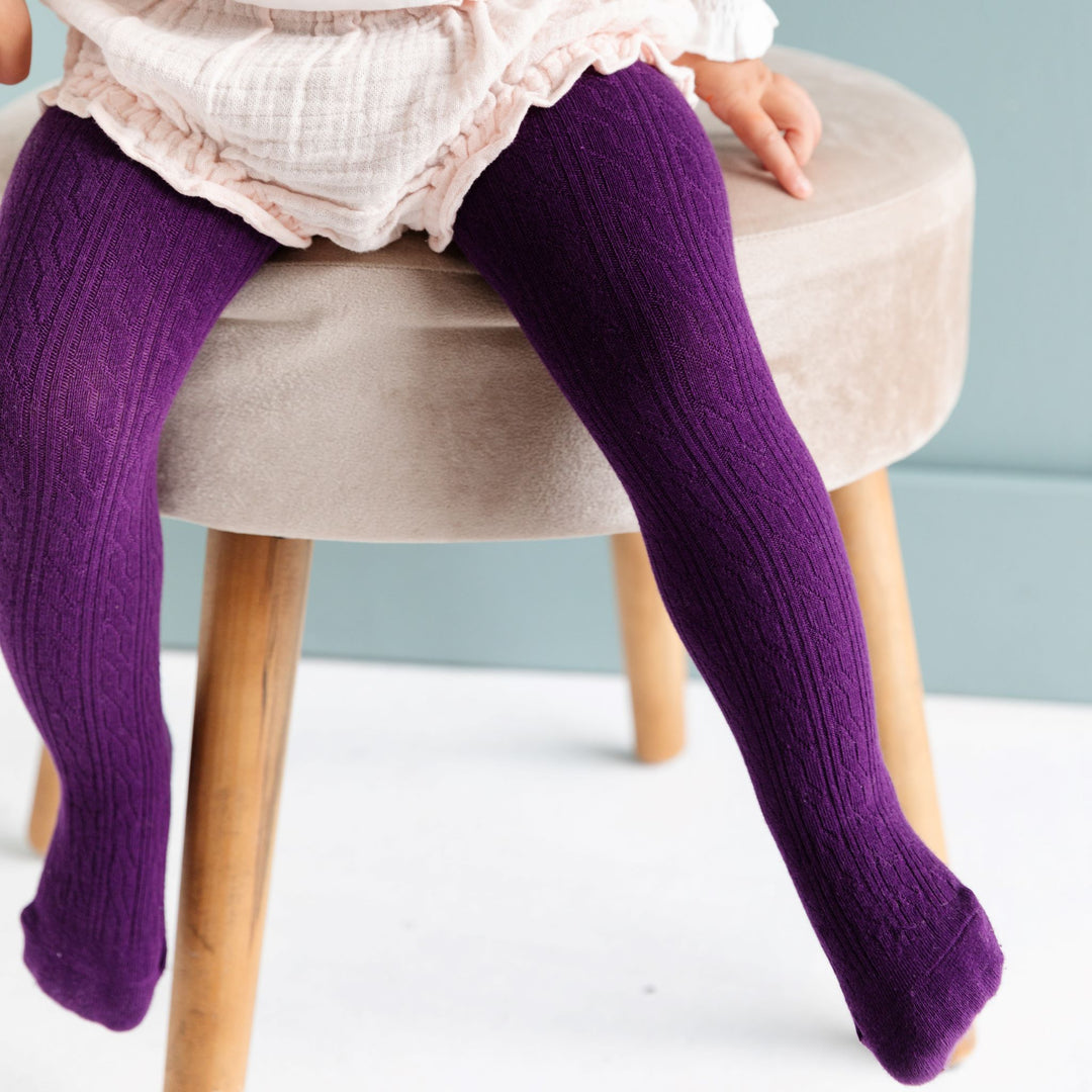 toddler wearing dark purple cable knit tights on stool