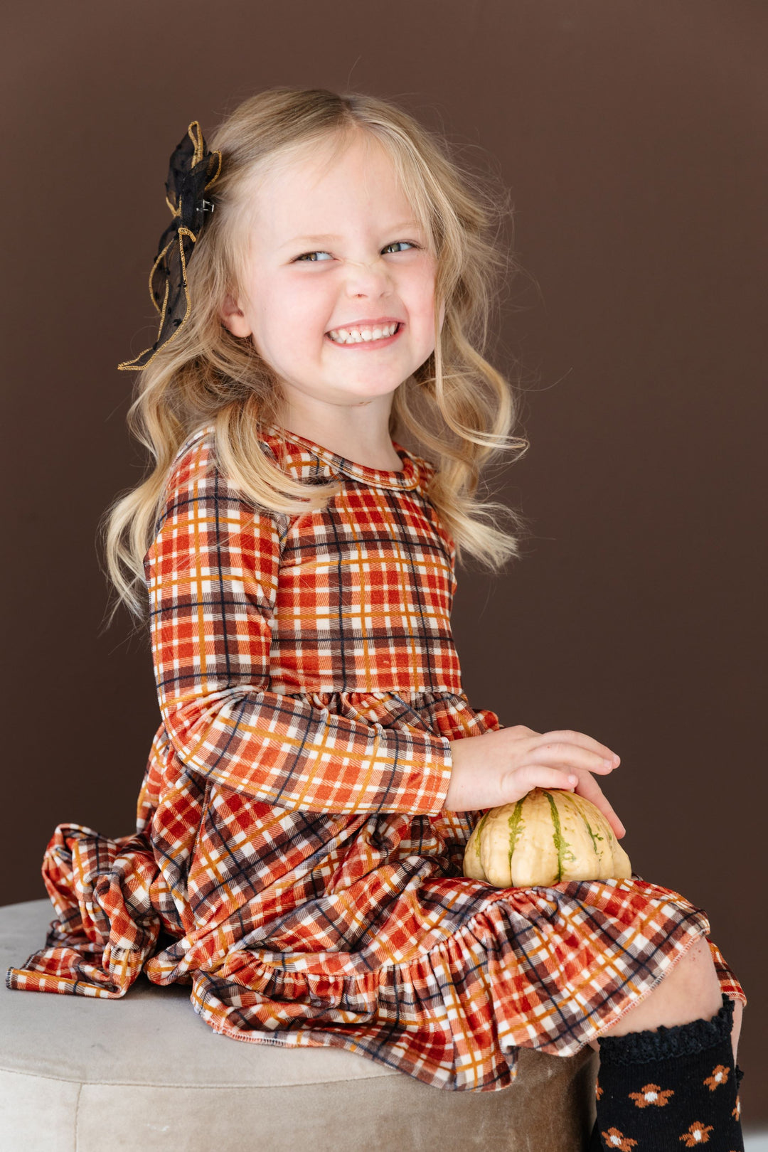 little girl in plaid twirl dress in fall shades, matching sheer black bow and black floral knee highs for Thanksgiving