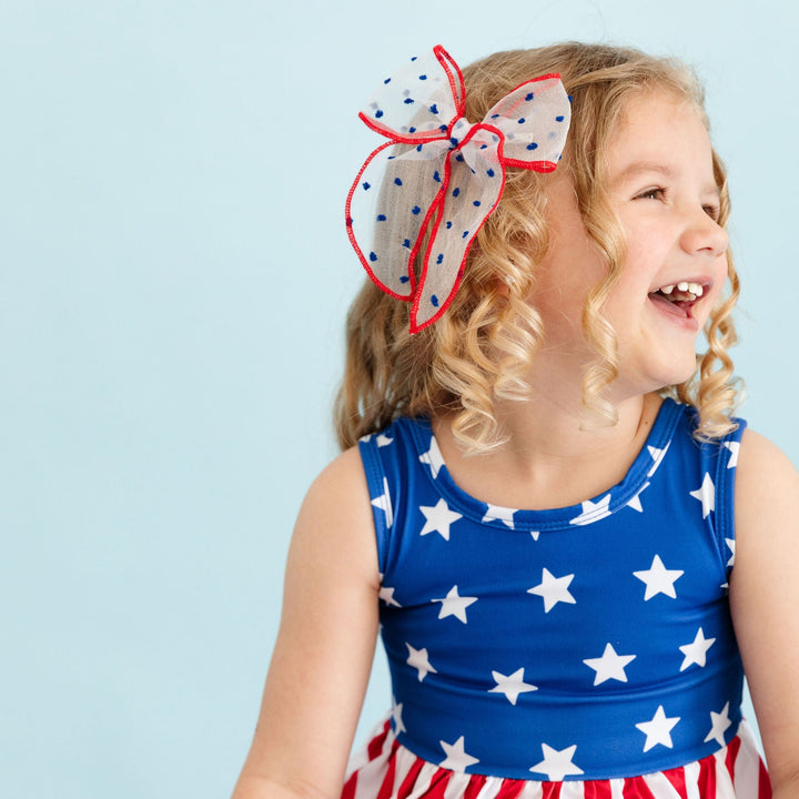 smiling little girl wearing american flag dress and matching sheer red, white and blue hair bow