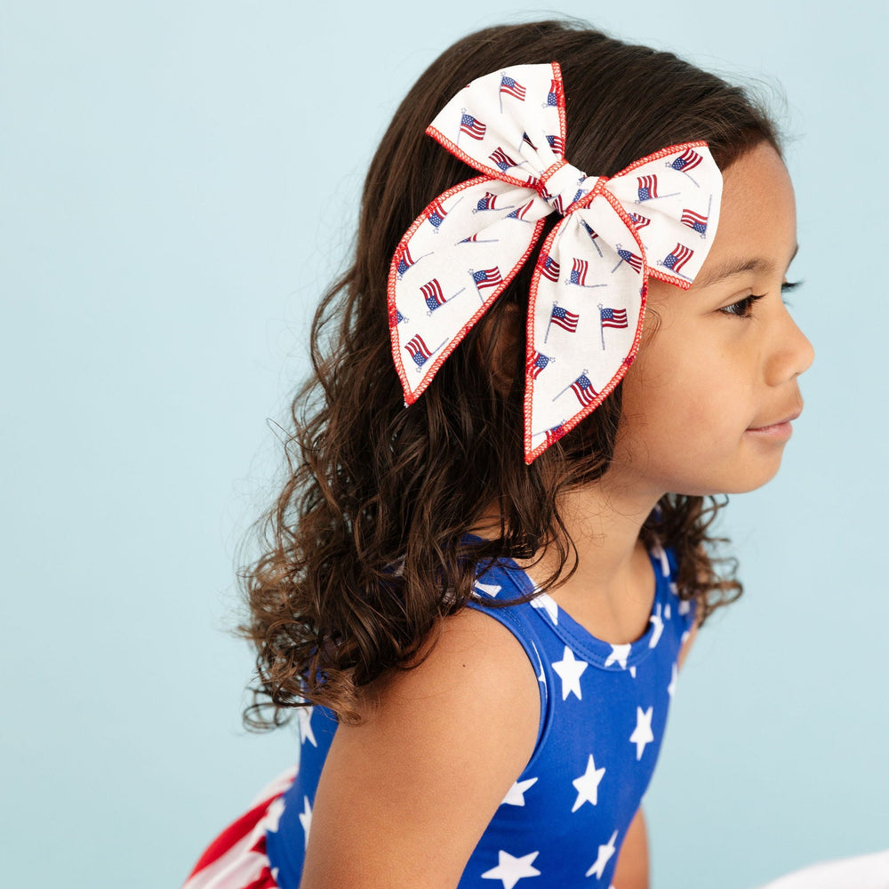little girl wearing american flag inspired dress with matching usa flag print hair bow