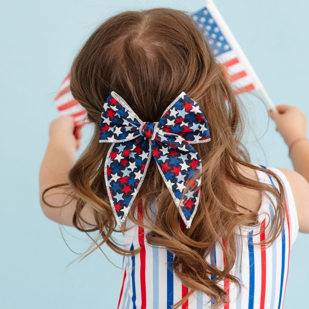 little girl wearing 4th of july start print hair bow and red, white and blue striped 4th of july dress