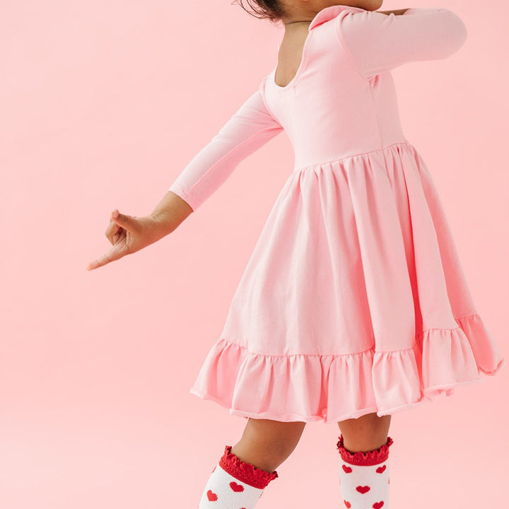 girl twirling in light pink cotton twirl dress and valentines heart knee high socks