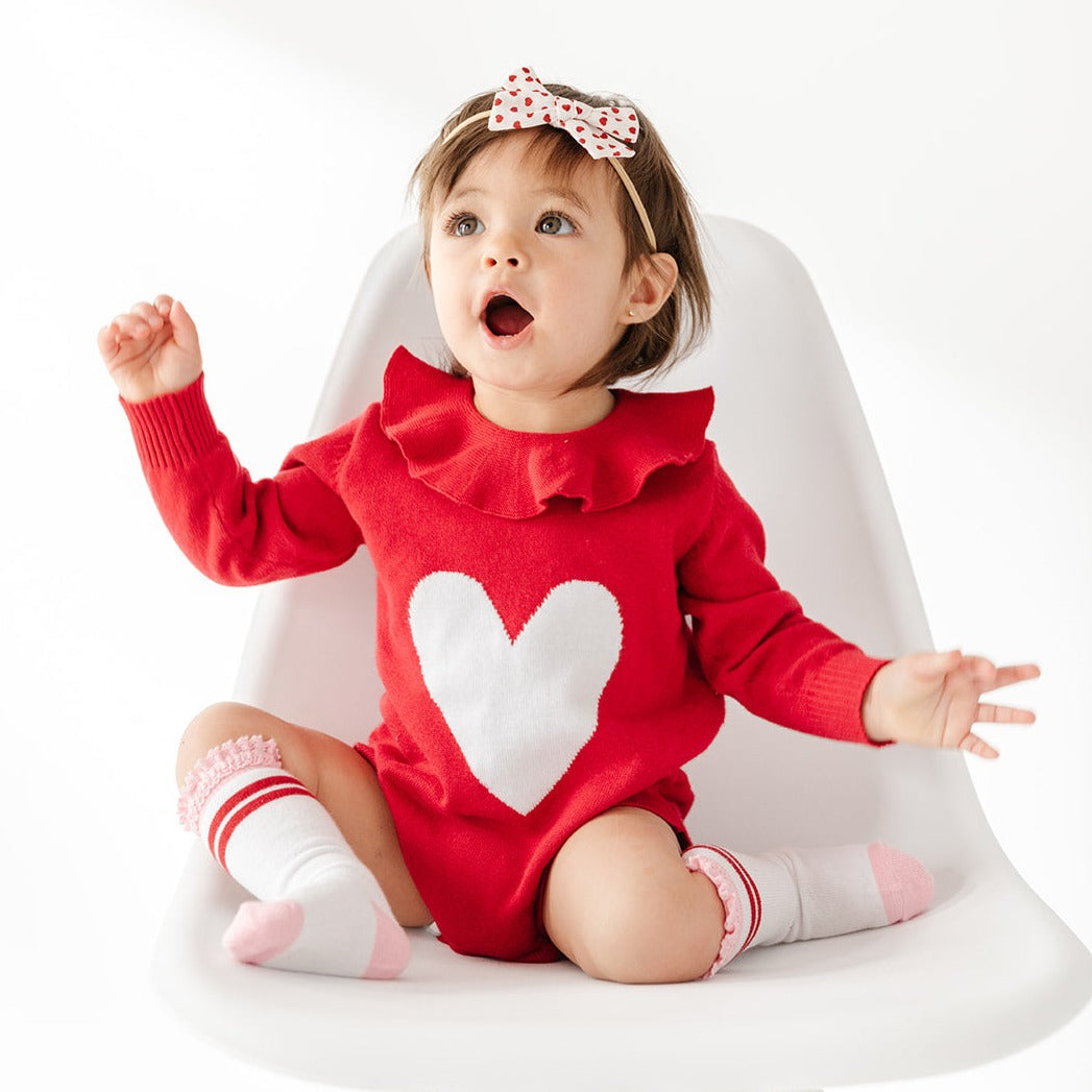 baby girl in knit romper with big heart for valentine's day and matching stripe knee high socks with lace