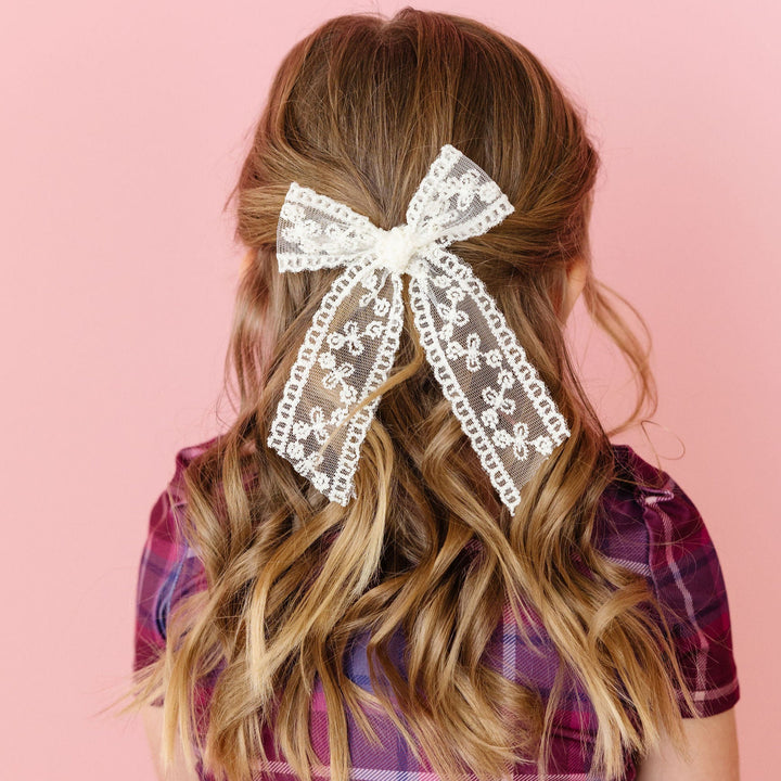 Girl wearing a plaid dress with a large lace hair bow on a pink background