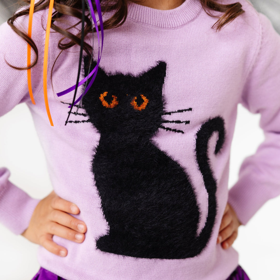 close-up of fluffy black cat design with sparkly orange eyes on lavender cotton knit sweater layered over purple witch themed twirl dress for Halloween