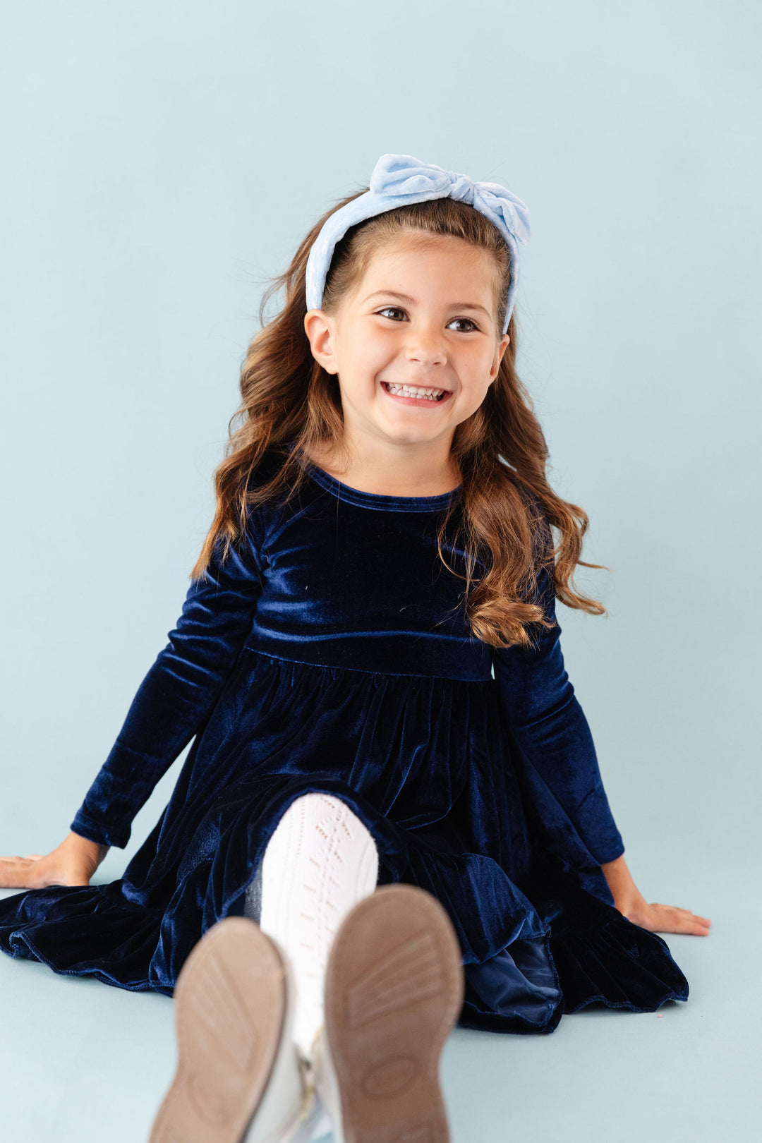 little girl sitting in midnight blue velvet charm dress and matching winter blue velvet headband