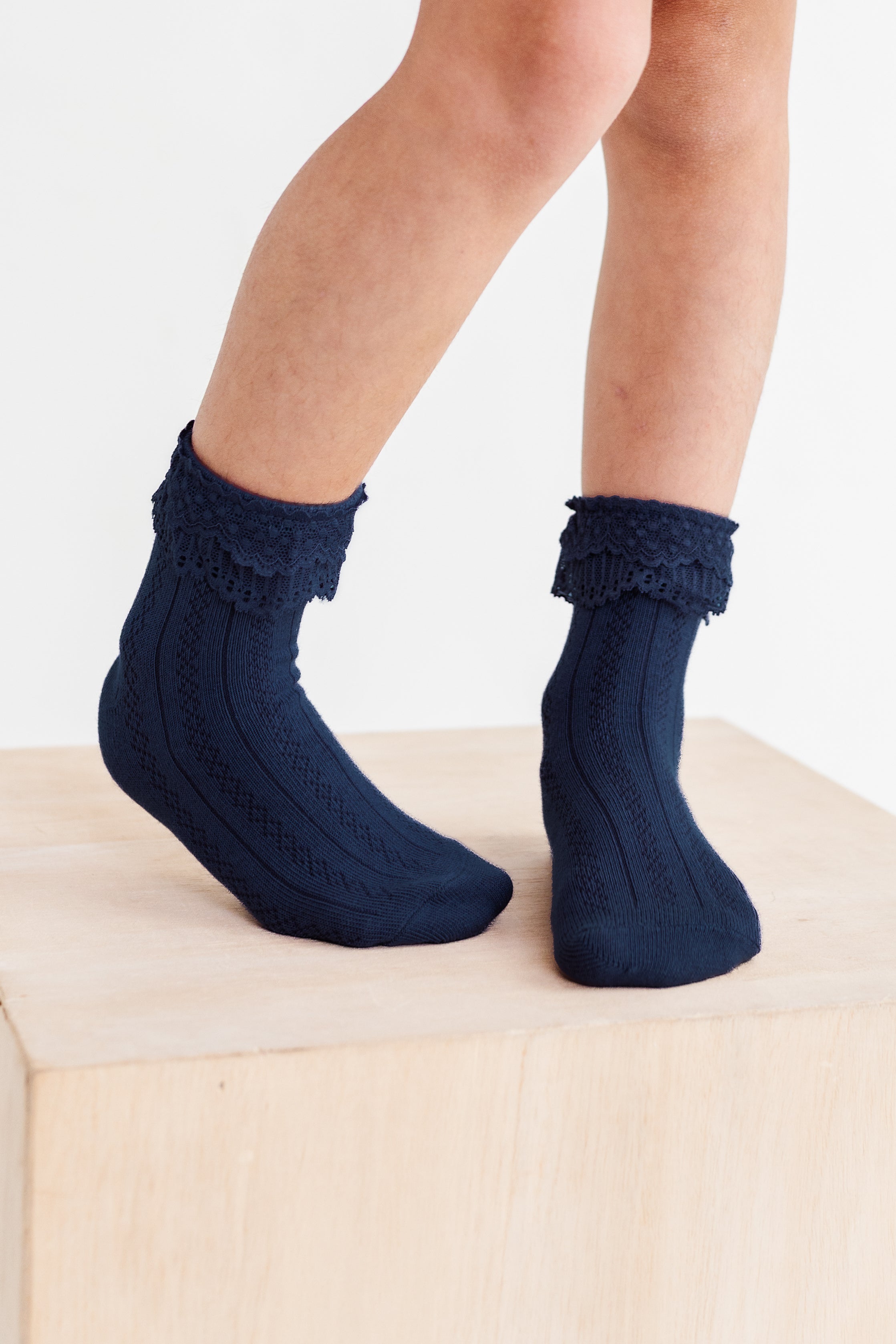 little girl standing on wooden box in navy ankle socks with lace trim