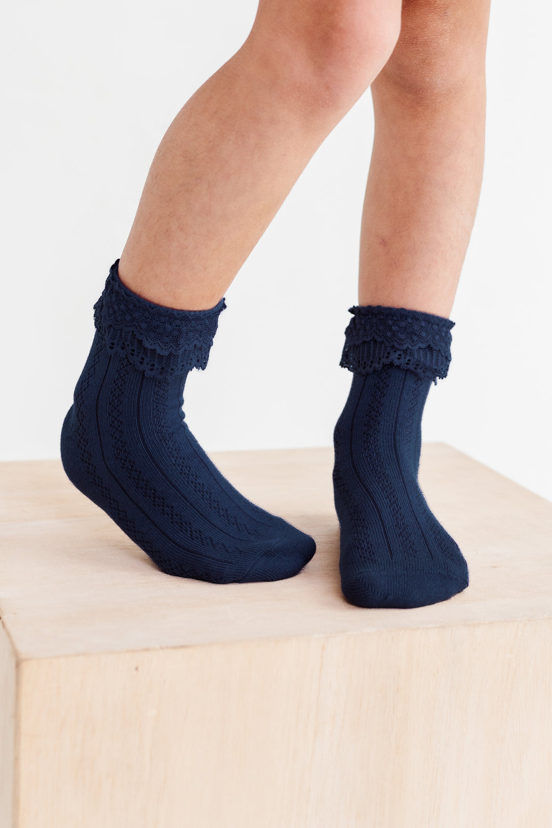 little girl standing on wooden box in navy ankle socks with lace trim