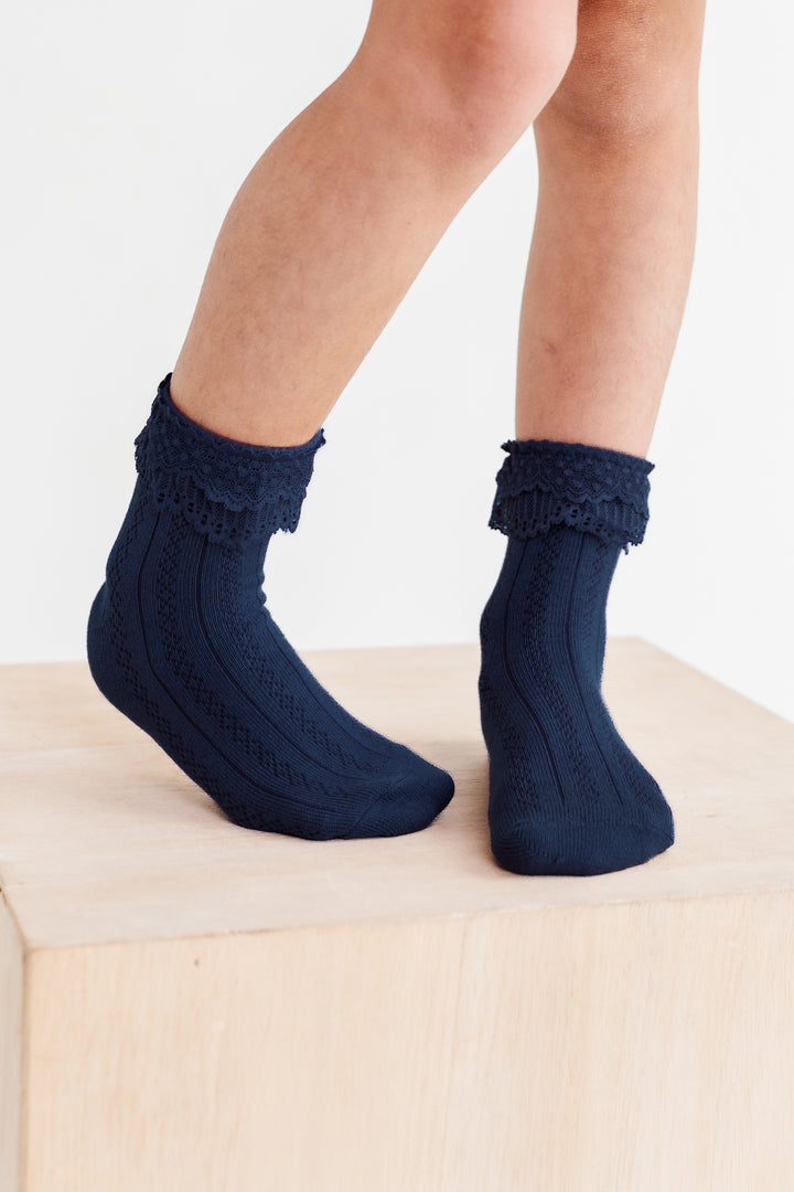 little girl standing on wooden box in navy ankle socks with lace trim