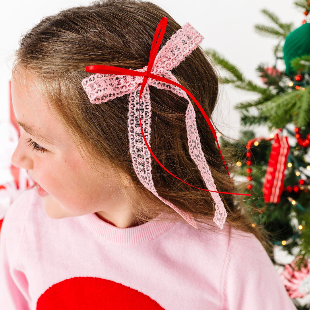 Child wearing a pink headband with a red bow, standing in front of a decorated Christmas tree.
