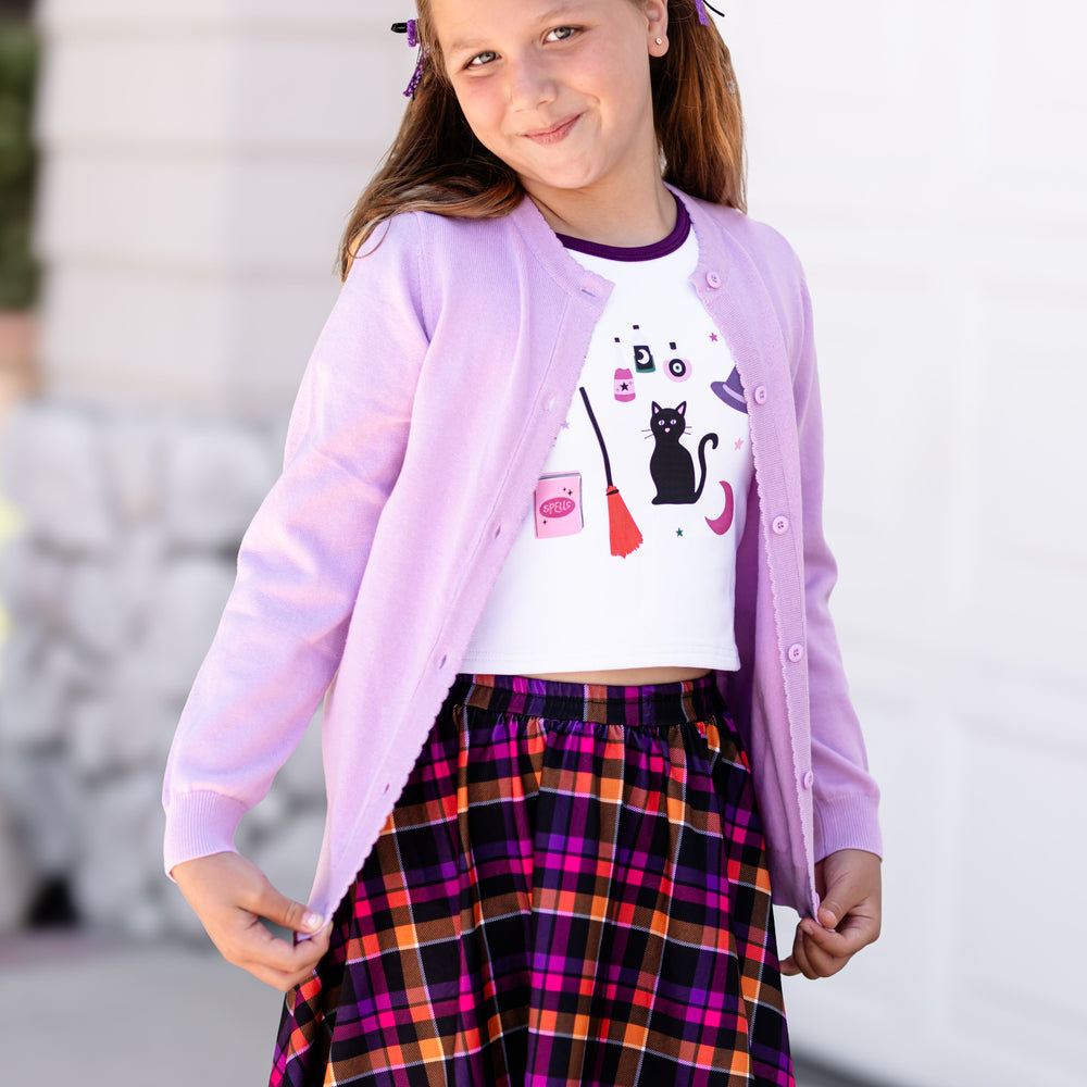 little girl in light purple cotton knit sweater over witchy tee and plaid skort in Halloween shades