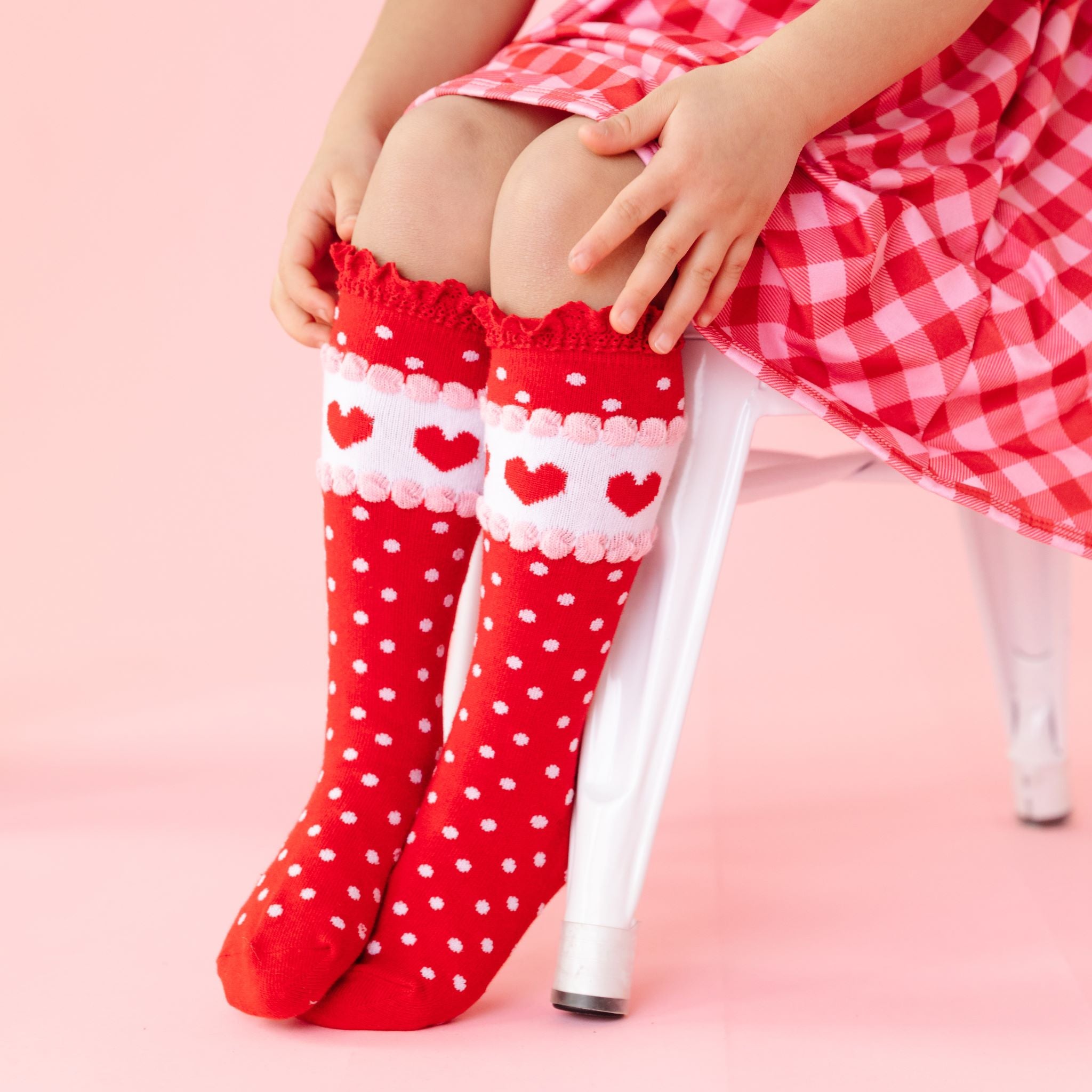 little girl in Valentine's inspired red lace top knee high socks with polka dots and heart detail paired with matching red and pink gingham dress