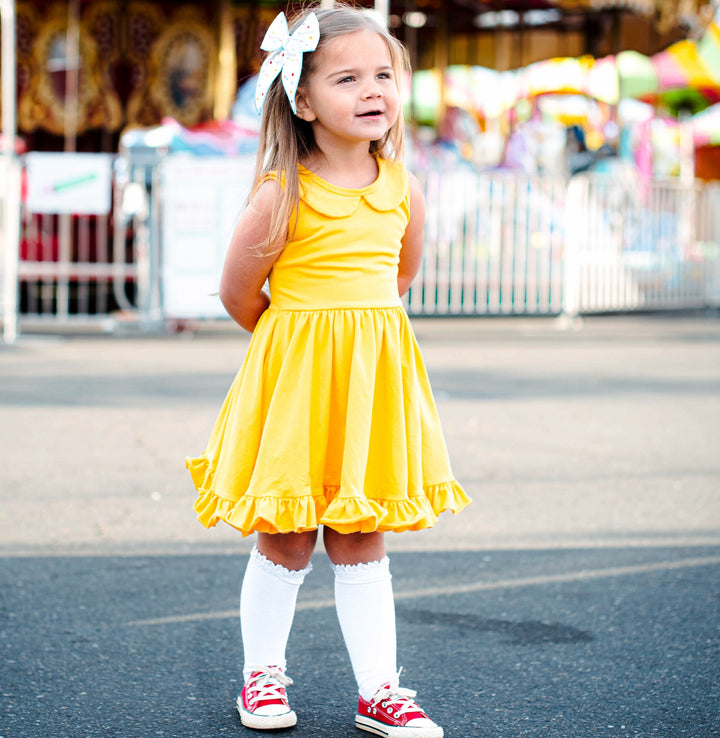 little girl at carnival wearing bright yellow tank top dress and white knee socks and red sneakers