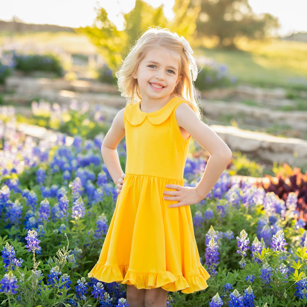 little girl standing in flowers wearing bright yellow sleeveless summer dress