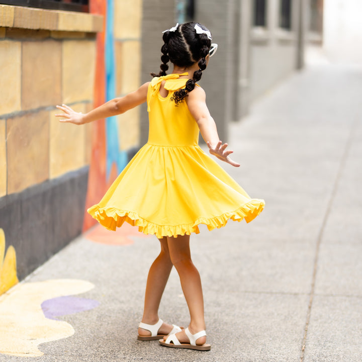 little girl twirling on sidewalk in bright yellow tank top dress