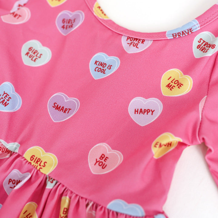 closeup of multicolor conversation hearts with words of affirmation printed on pink Valentine's Day dress