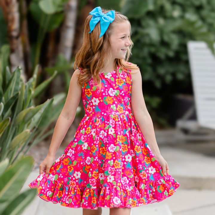 little girl in pink tropical floral print summer dress and bright blue hair bow