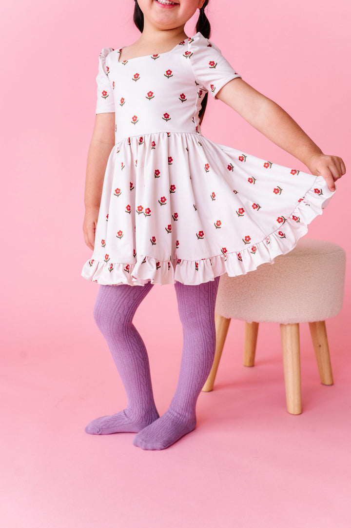 young girl wearing cream floral twirl dress with floral design in rust and amethyst with matching purple cable knit tights