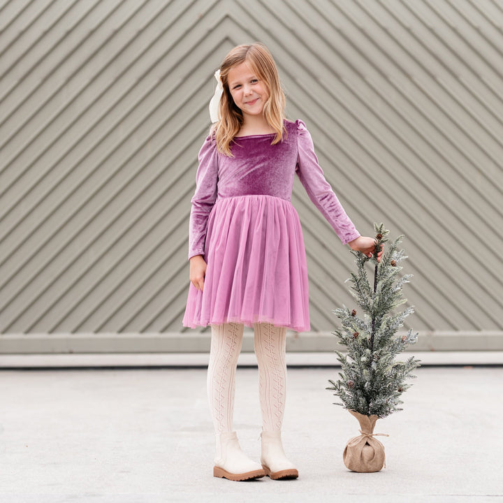 girl holding Christmas tree in purple velvet and tulle party dress with coordinating vanilla satin bow and open knit tights