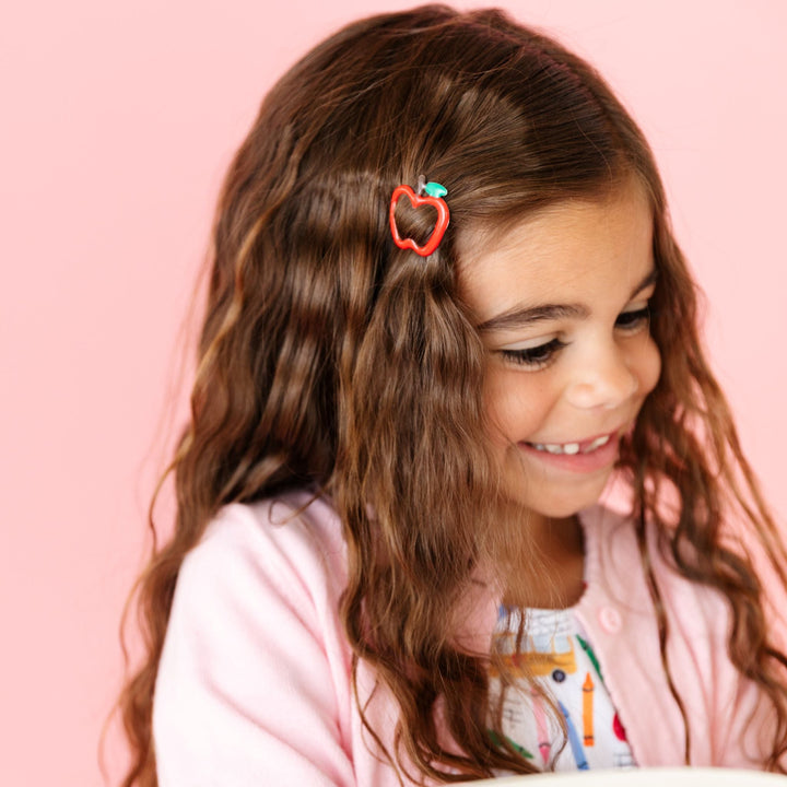 little girl holding book in back to school themed outfit and matching red apple hair clip