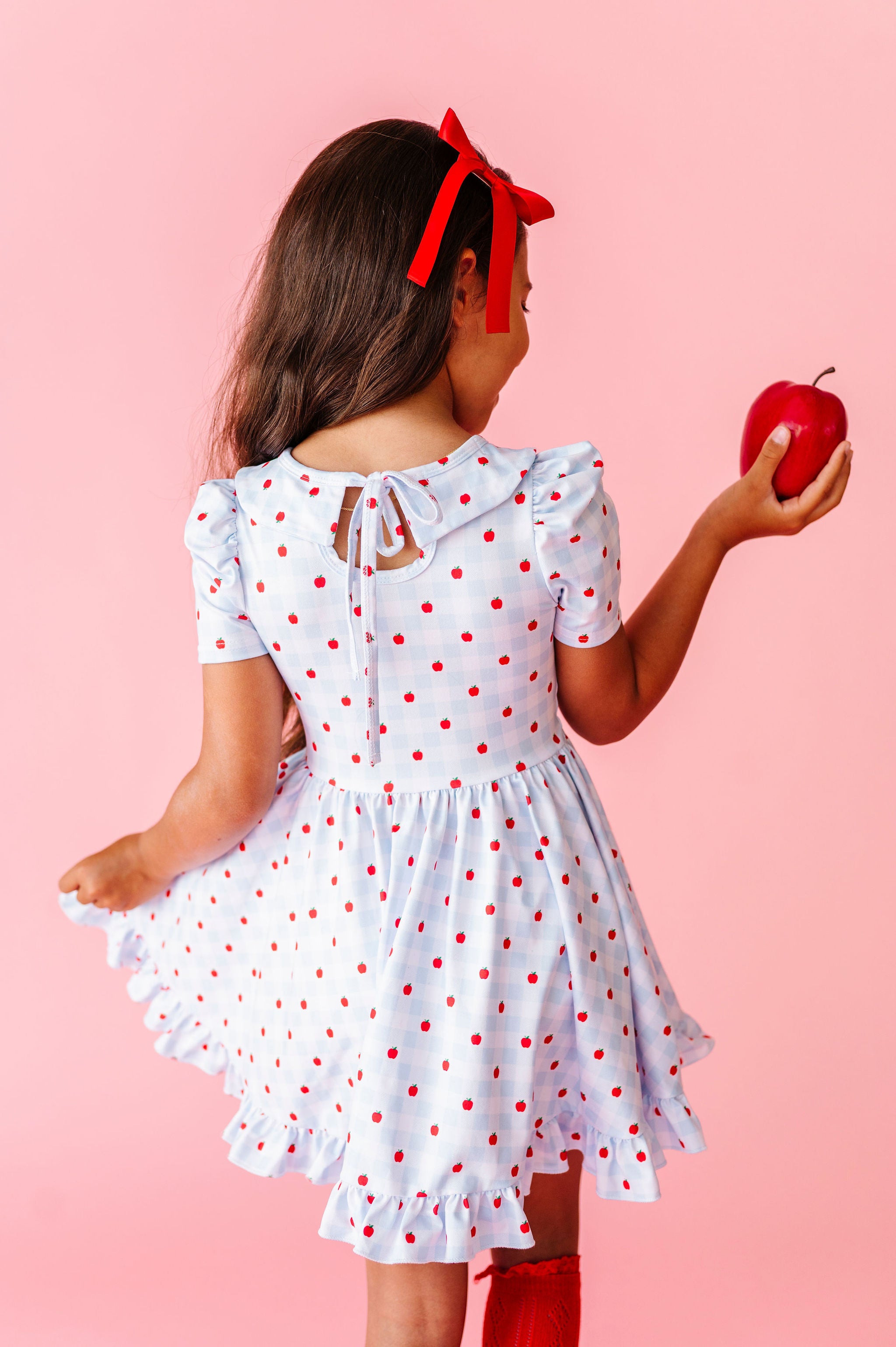 girl wearing light blue and white back to school dress with bow tie on back and red apples