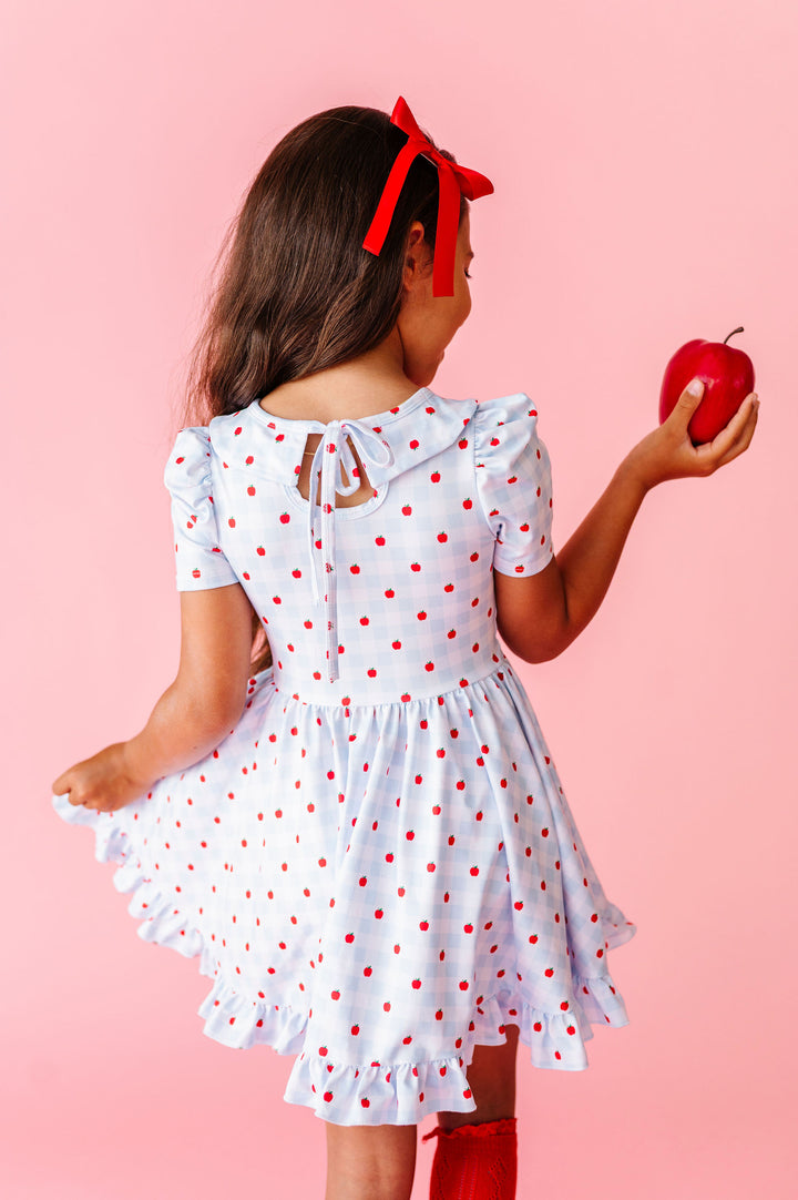 girl wearing light blue and white back to school dress with bow tie on back and red apples