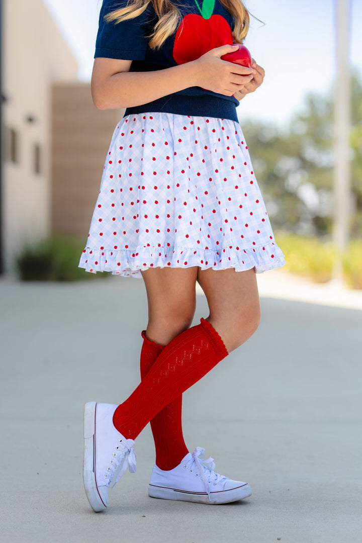 girl in blue and white gingham apple print twirl dress and navy sweater with red apple paired with bright pointelle lace top knee socks