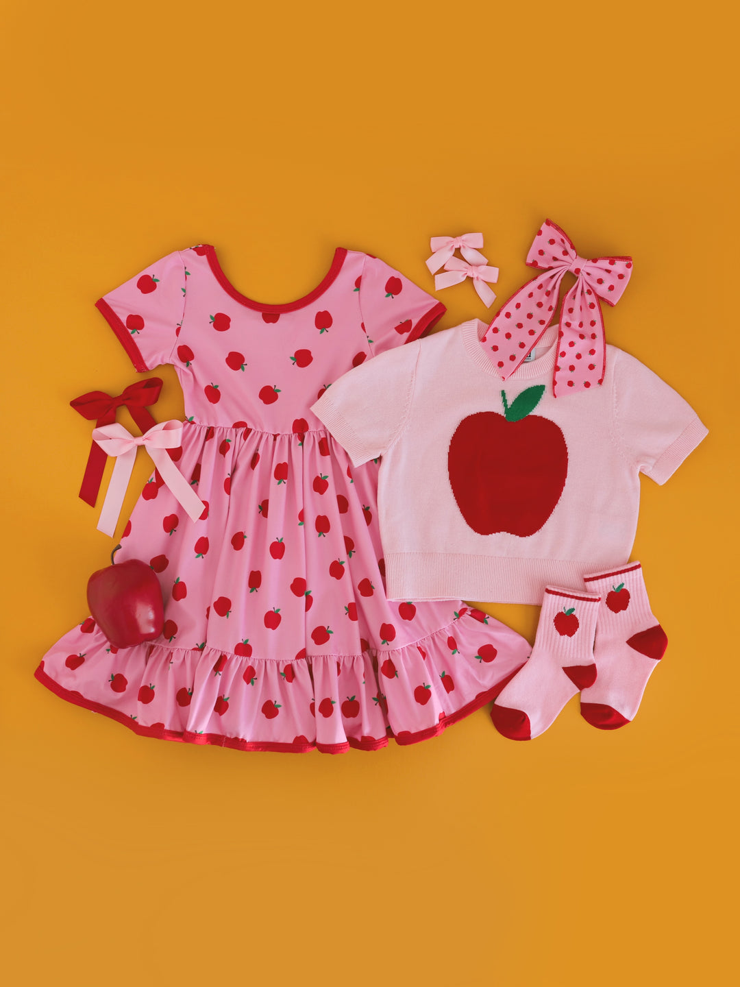 girls' apple themed back to school outfit with pink apple twirly dress, pink short sleeve apple sweater, apple crew socks and coordinating matching hair bows