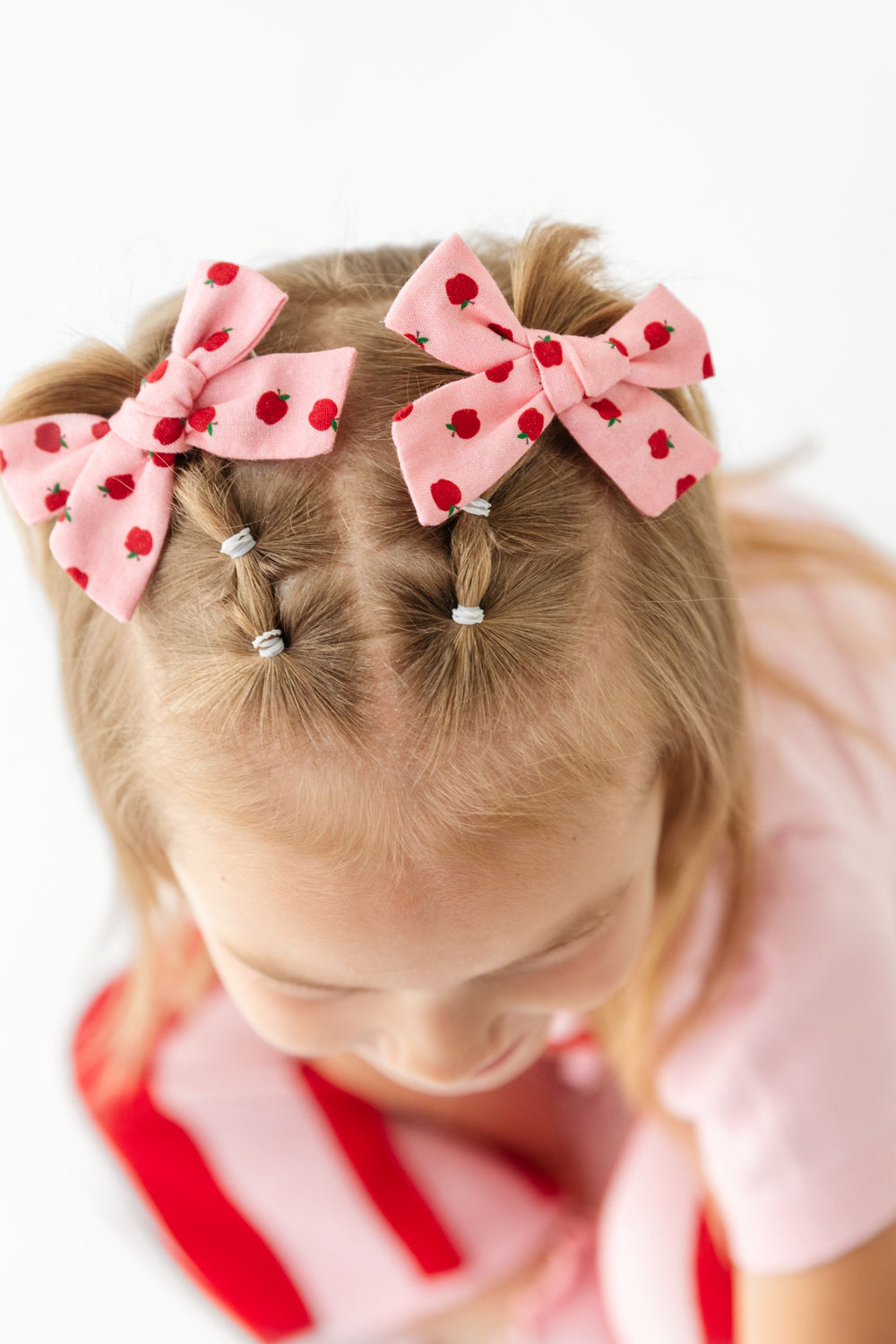 little girl in apple print pigtail bows on clips and matching sweater set