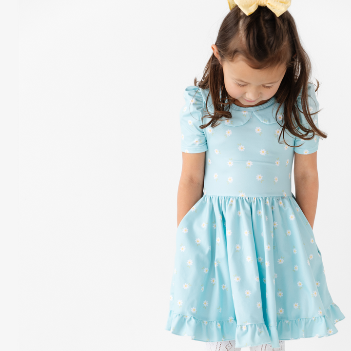 little girl wearing light blue and daisy print twirl dress and matching yellow hair bow