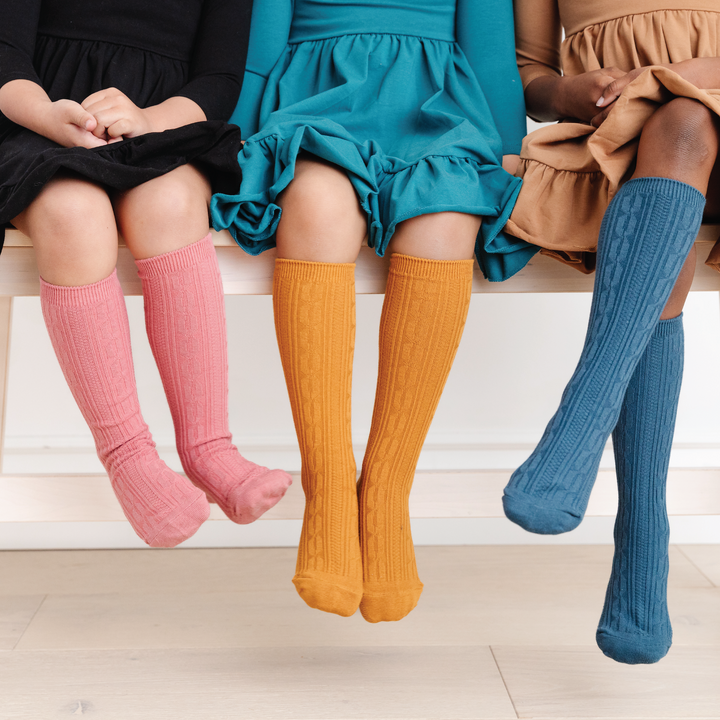 3 girls wearing cable knit knee high socks for girls in pink, mustard and blue