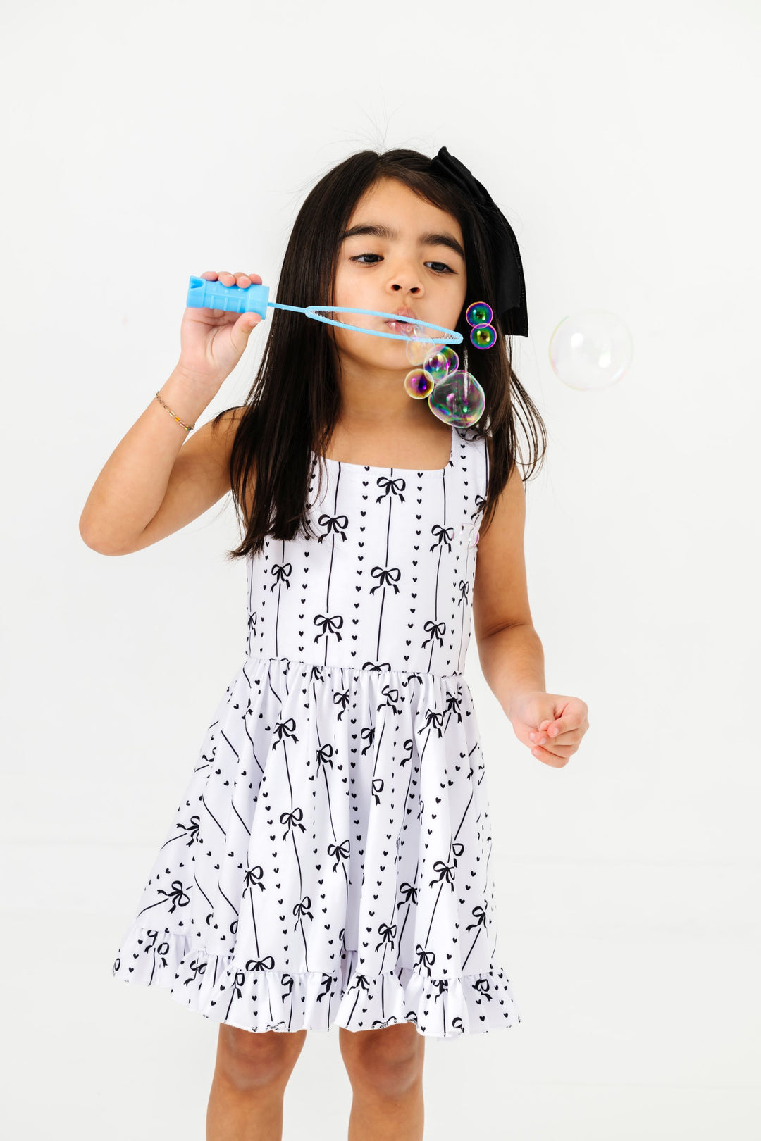 little girl blowing bubbles with white with black bow design summer tank twirl dress and matching black satin hair bow