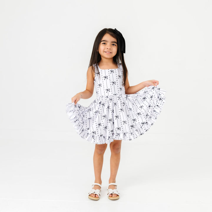 little girl in white sleeveless twirl dress with black bow and heart pattern paired with white sandals for summer