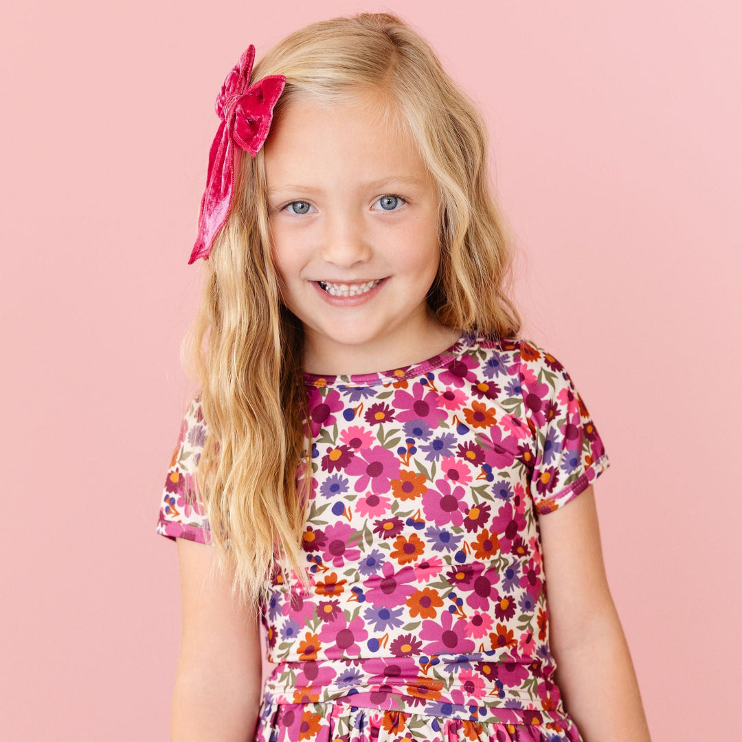 Young girl wearing a colorful floral dress against a pink background