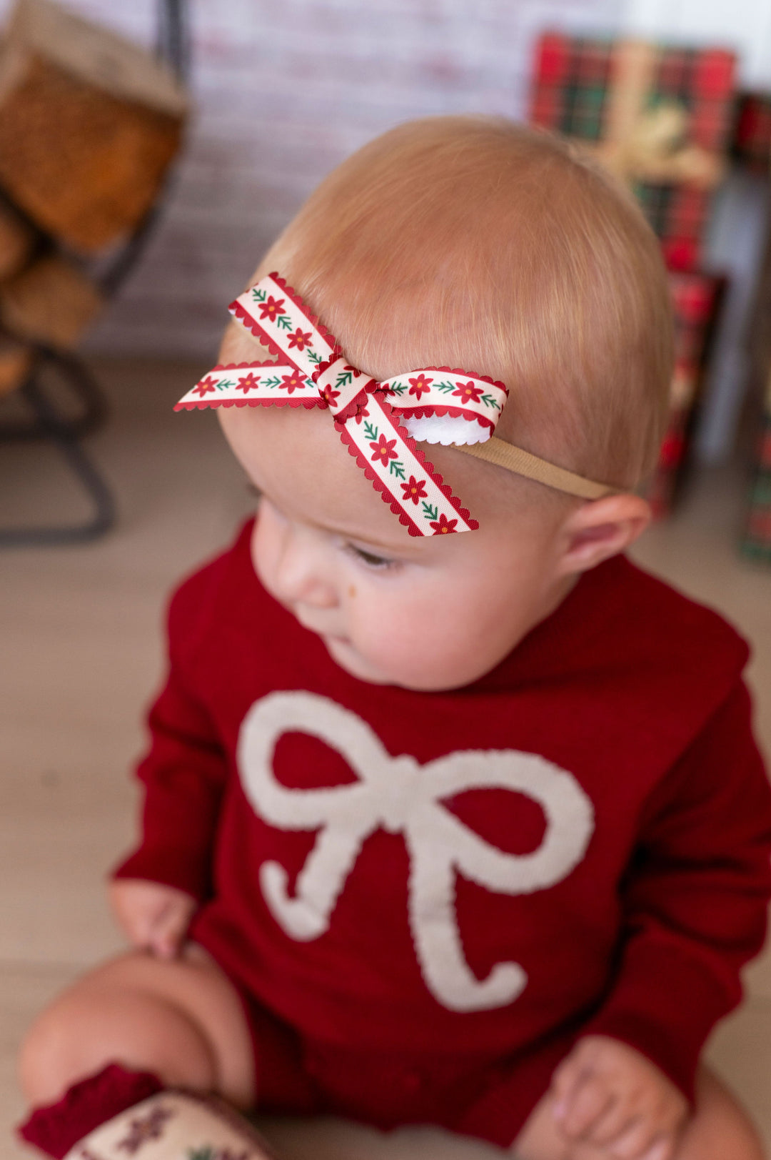 baby sitting on wood floor wearing crimson bow knit outfit and poinsettia ribbon headband bow