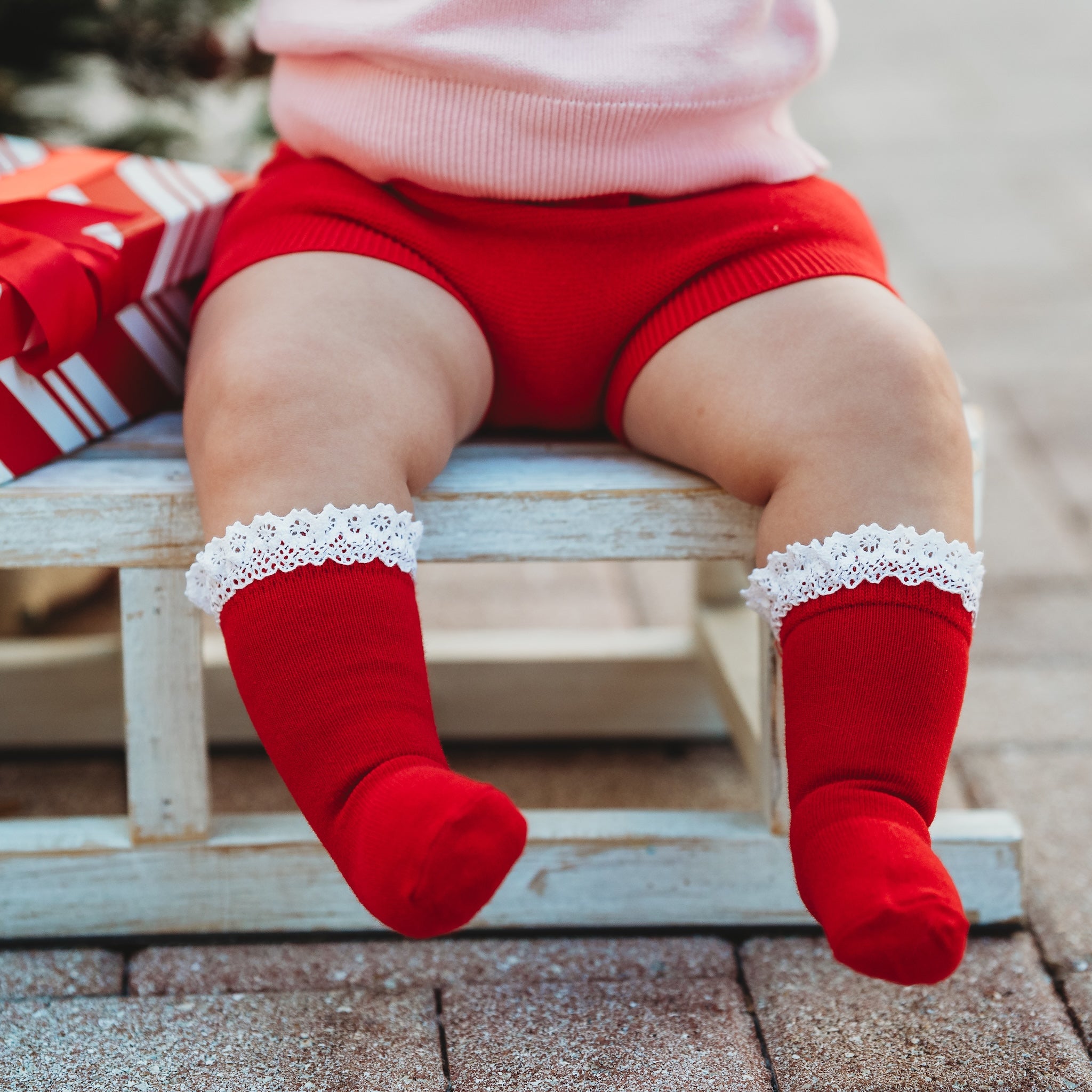 baby girl sitting on sled in red knee socks with white lace trim paired with Christmas sweater set