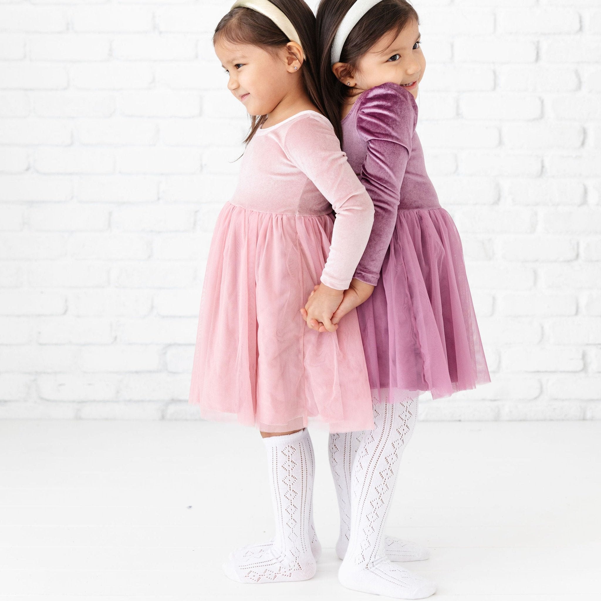 little girls wearing pink and purple party dresses with white pointelle knee high socks and tights