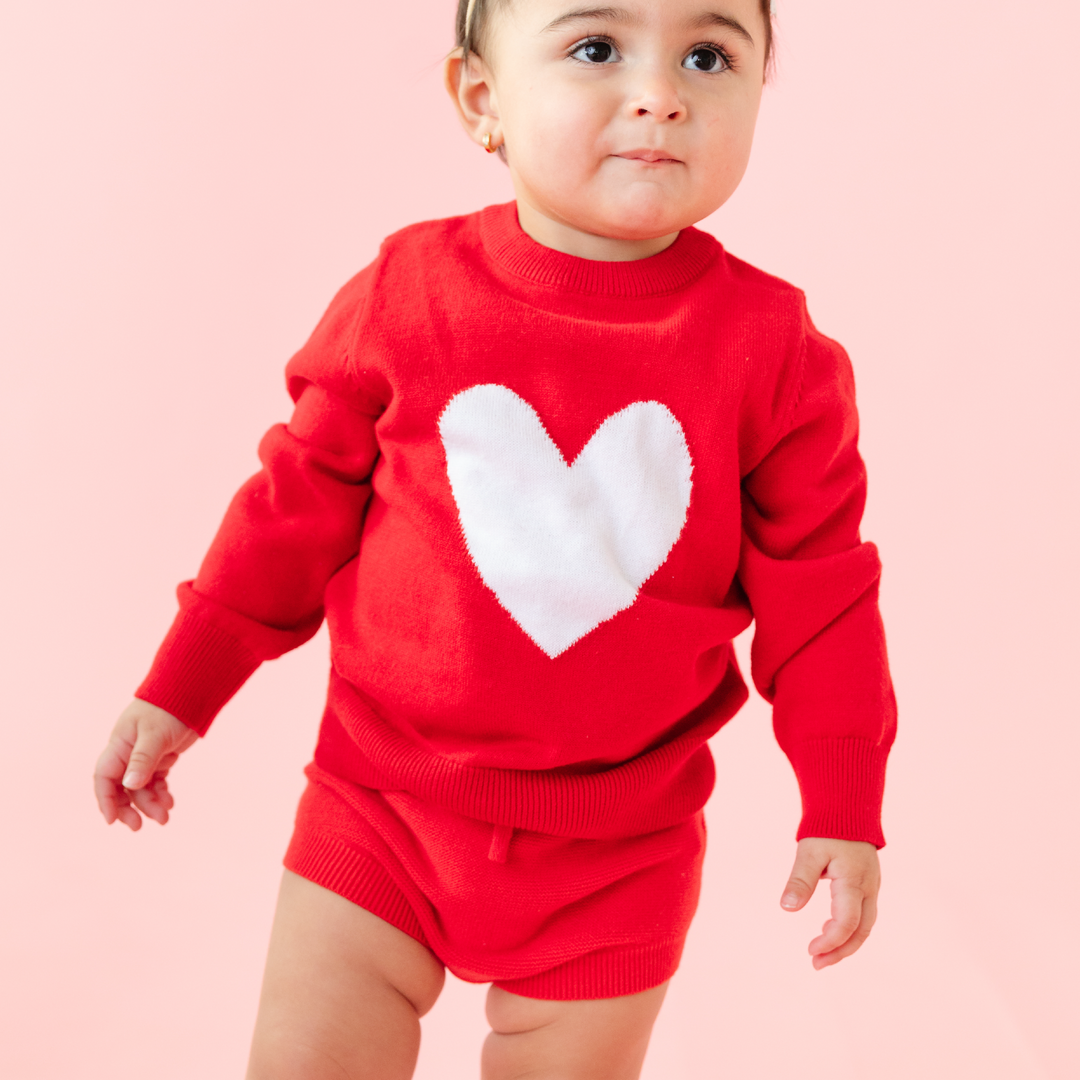 baby girl in bright red sweater with white heart and matching red knit bloomers