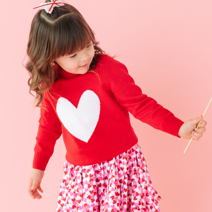 little girl wearing bright red sweater with white heart and confetti heart dress for Valentine's day