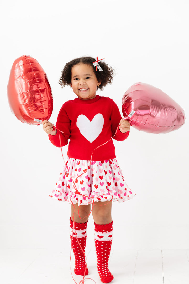 little girl in red, white and pink Valentine's look with matching lace bow, pullover heart sweater, heart twirl dress and knee high socks