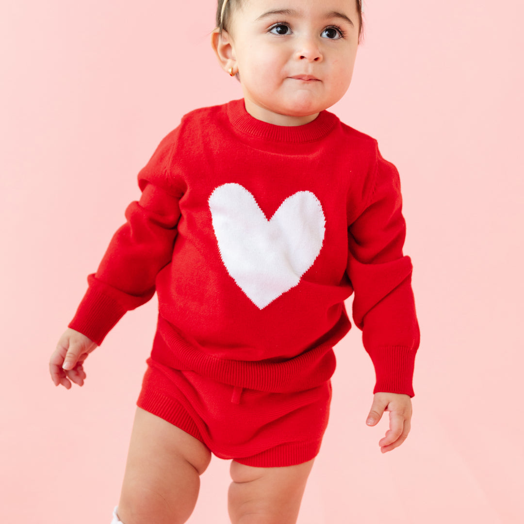 baby girl in bright red sweater with white heart and matching red knit bloomers