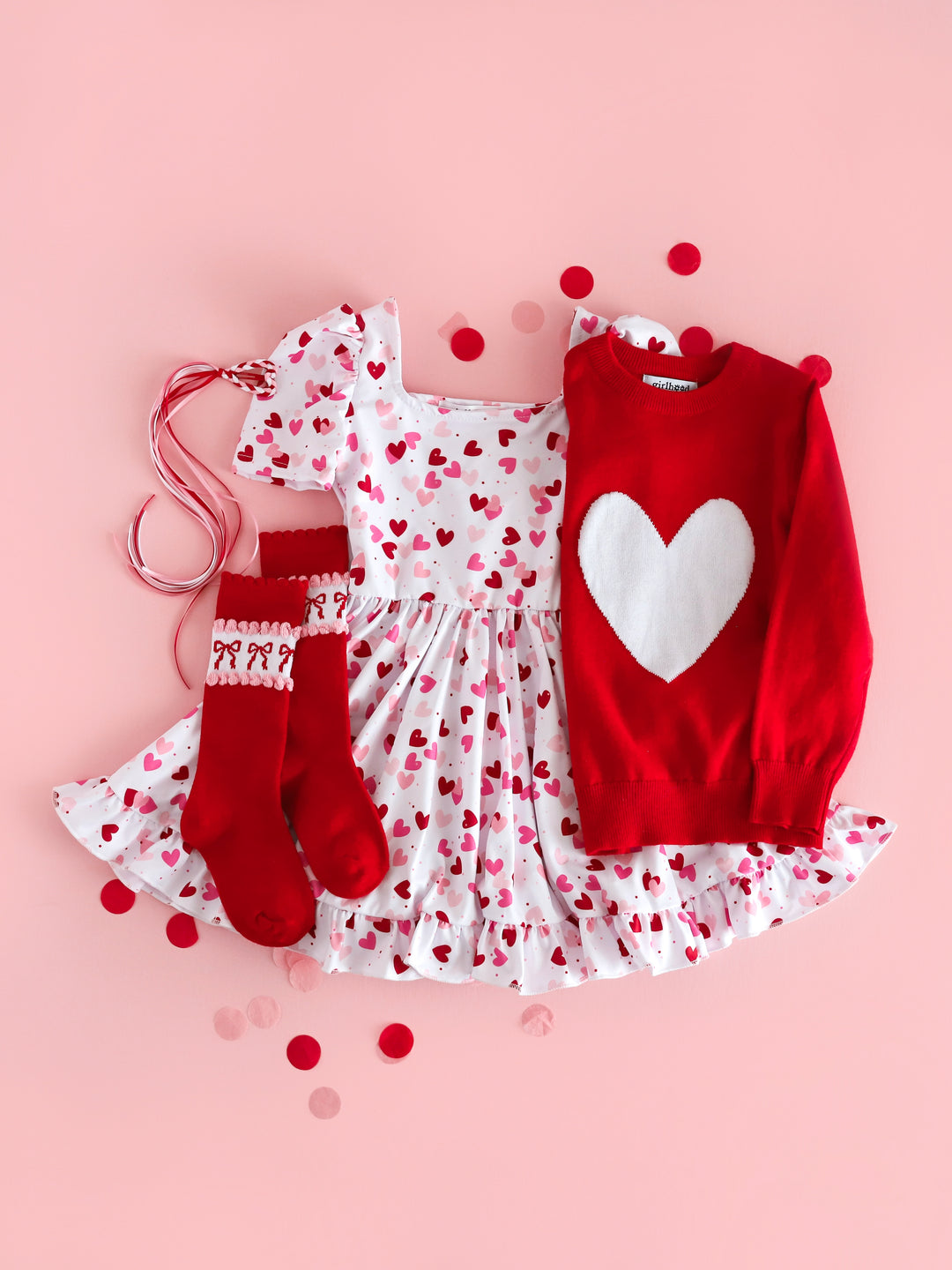 styled flatlay with girls confetti hearts twirl dress, bright red sweater with white heart design, matching red knee high socks with bow design and heart clip with matching ribbon streamers