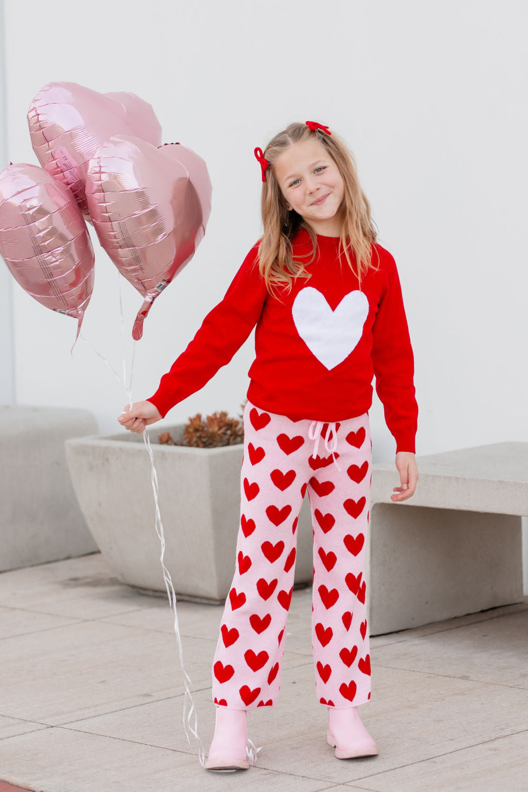 little girl holding heart ballons in red pullover knit sweater with white heart design and coordinating pink sweater pants with red hearts