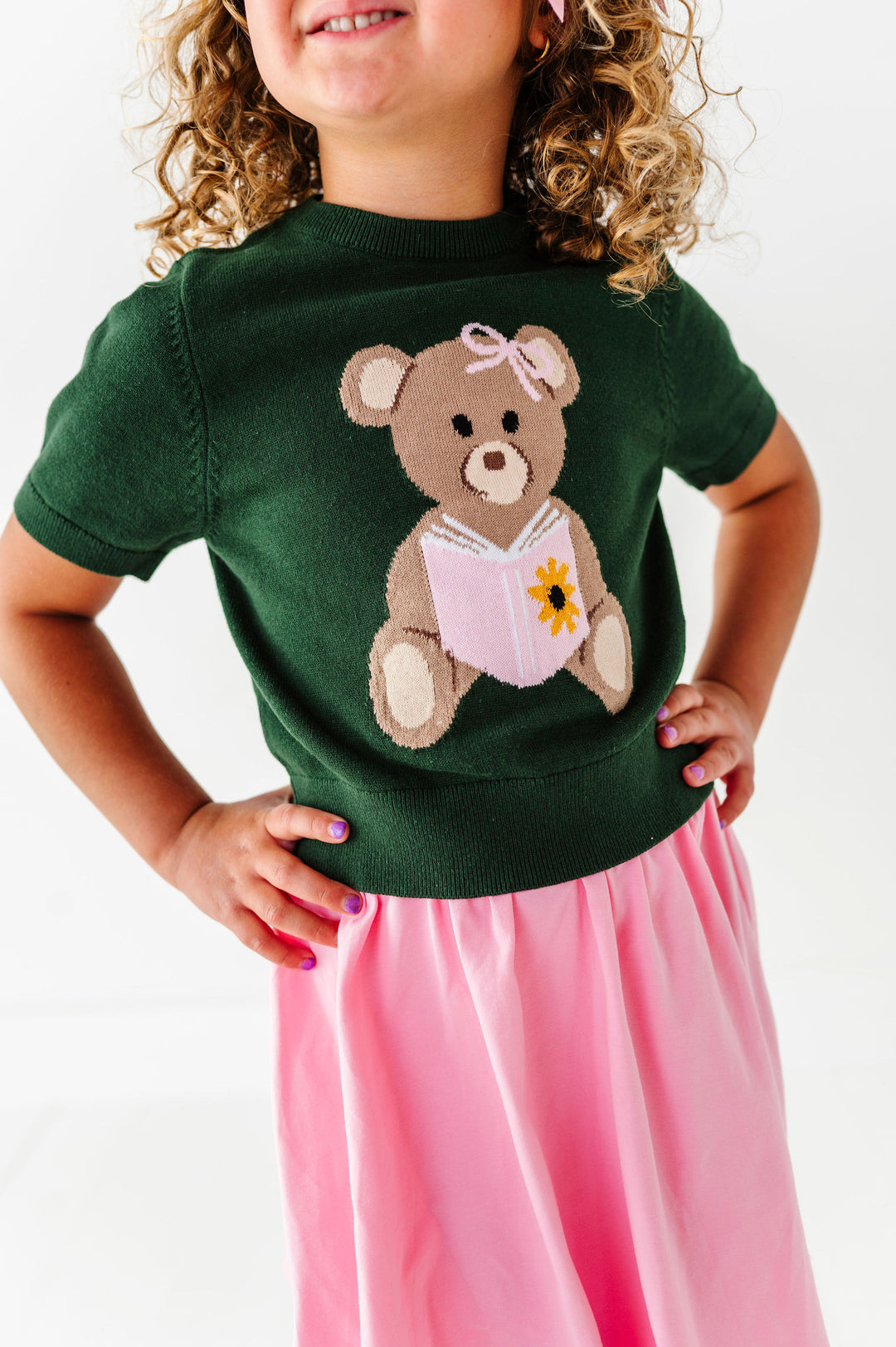 girl wearing a green knit shirt with a teddy bear design on a white background
