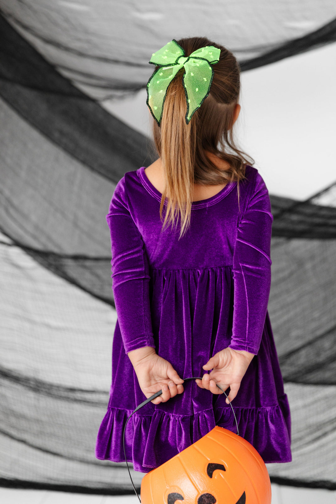 little girl wearing purple velvet dress with lime green beetlejuice hair bow